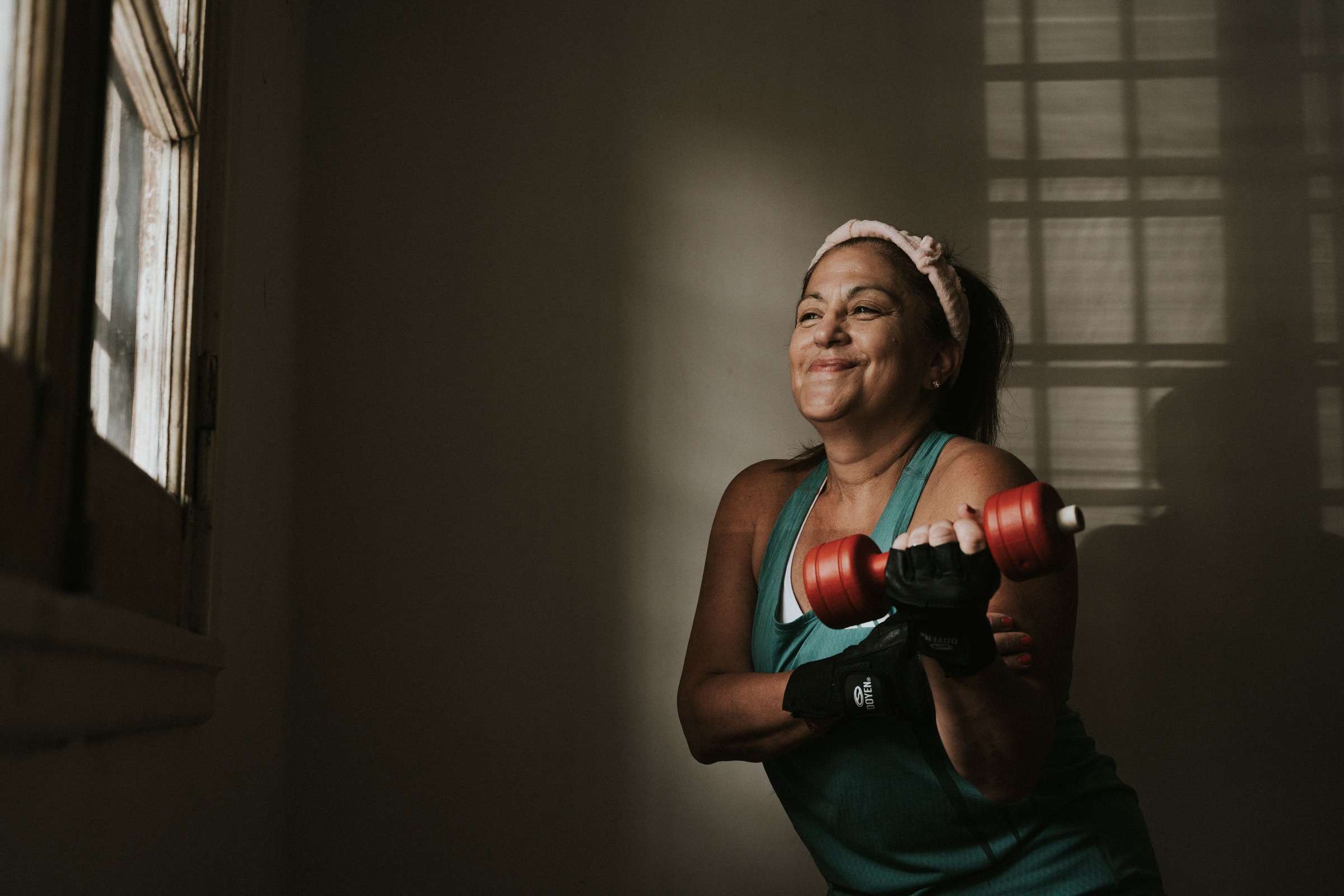 A woman lifting a red dumbbell beside a sunlit window