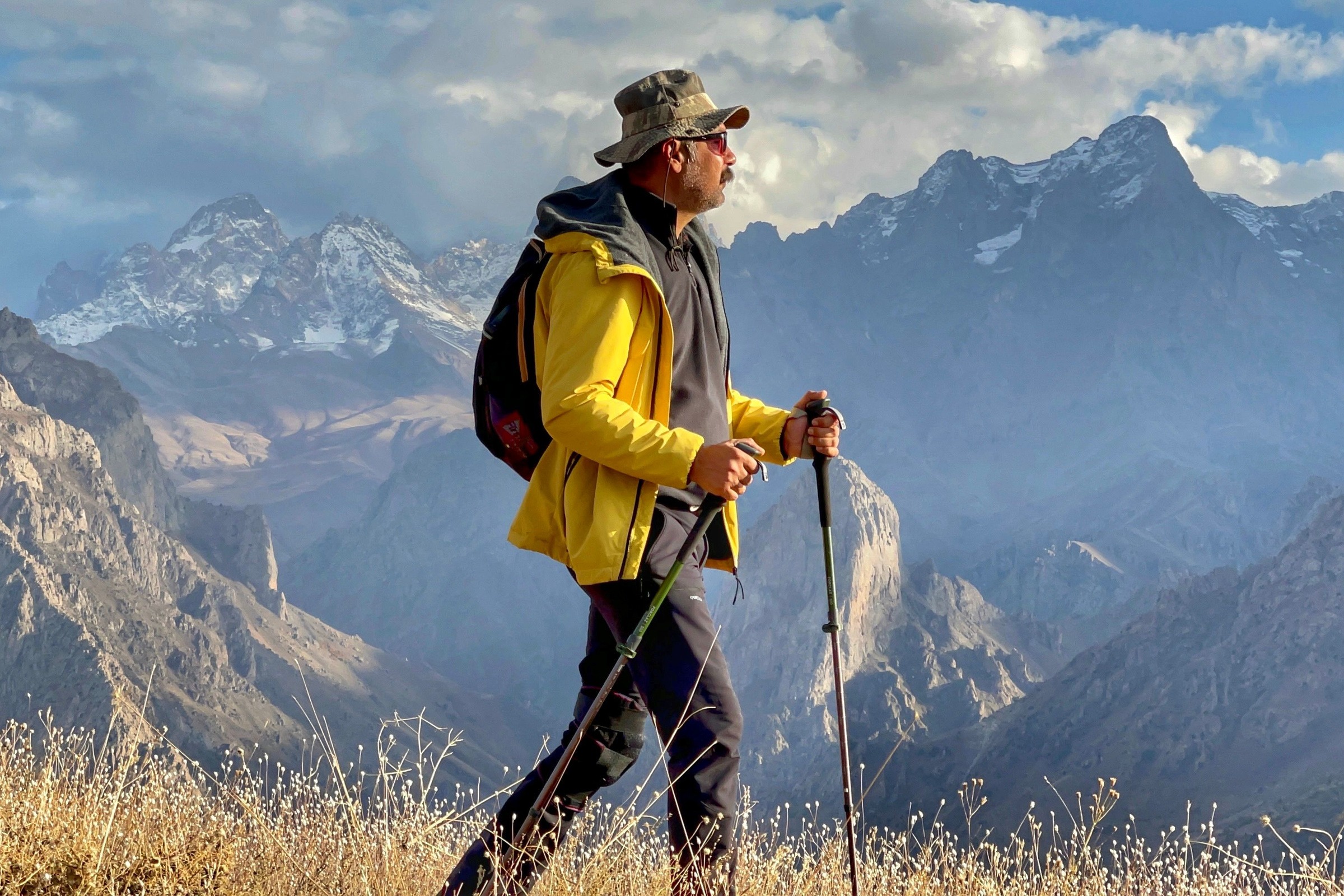 A hiker with trekking poles on a ridge above snowy mountains